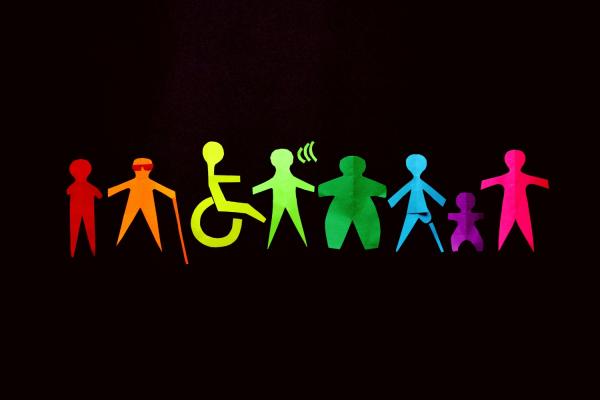 Colorful paper cutouts of diverse human figures, including representations of people with disabilities, a child, and various body types, stand side by side against a black background, symbolizing inclusion and diversity